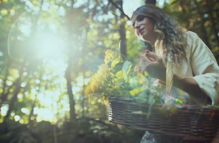 A young woman walks through the forest at midday holding a basket filled with flowers