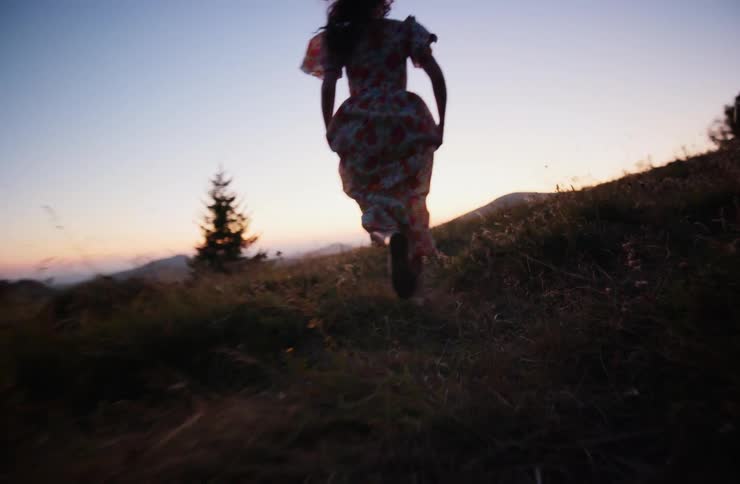 A woman in a dress runs through a grassy field at sunset