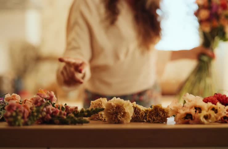 Colorful flowers arranged on wood as person positions bouquet in the background