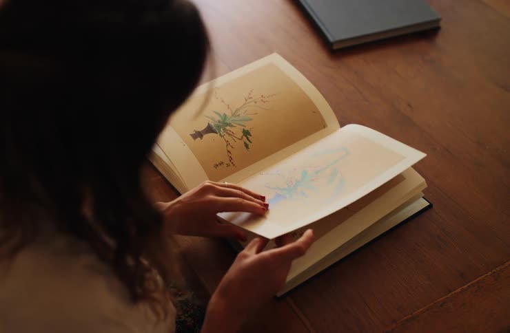 Woman flipping through an illustrated book with botanical drawings on the table
