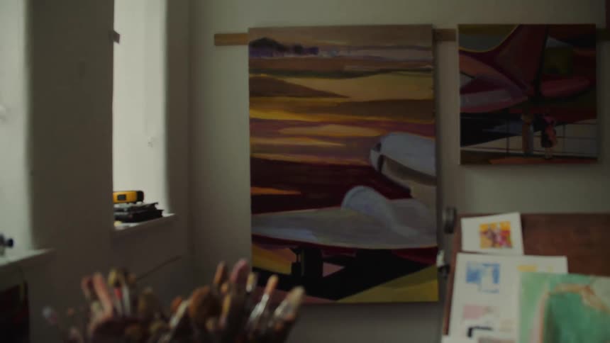 Painter working in the studio with an abstract landscape canvas in the background