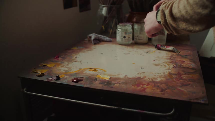 Close up of a female artist mixing paints on a large palette in an art studio during daytime