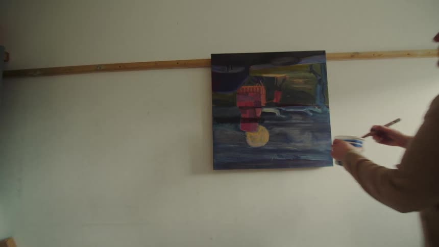 Woman in beige sweater paints on colorful canvas on white wall with wooden support