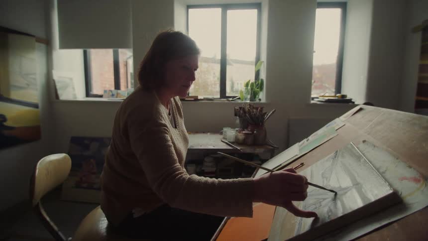 Painter working on her canvas inside a studio lit by large windows