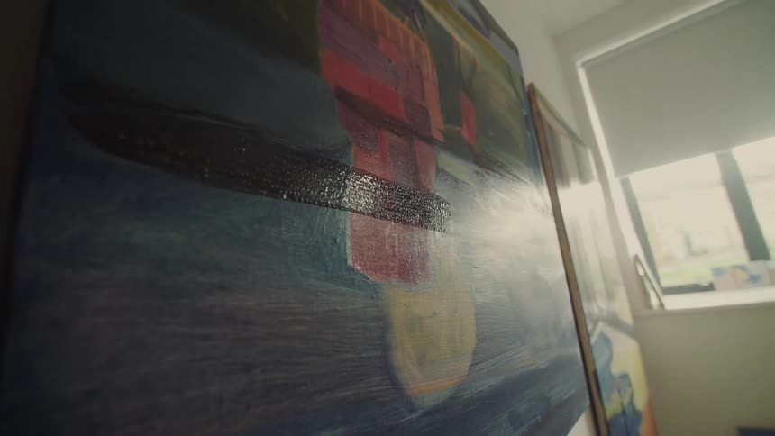 An artist applies dark paint to a large abstract canvas in a brightly lit studio