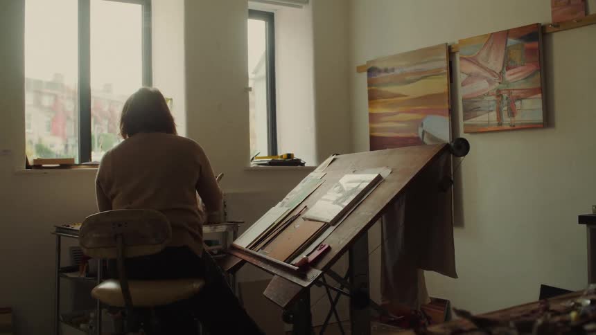 A female artist painting a small canvas on a stand in an art studio during daytime
