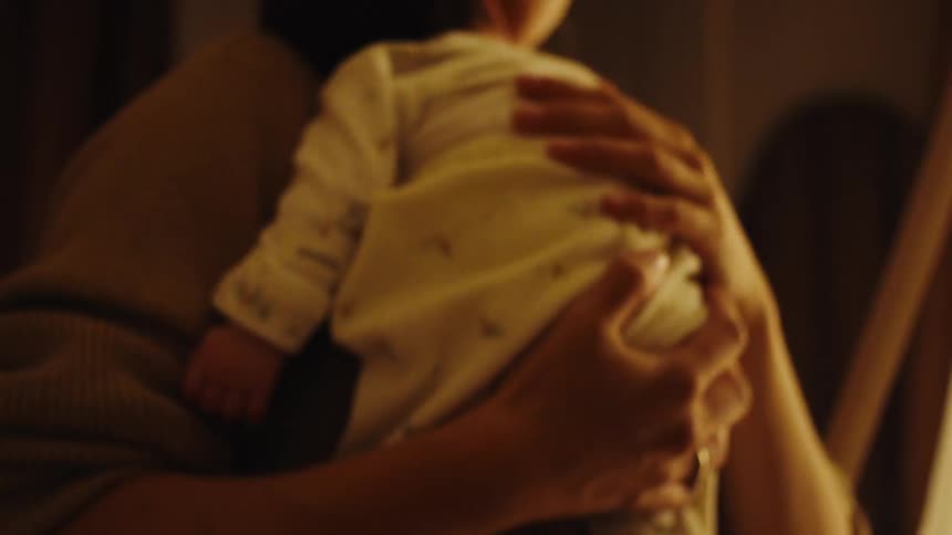 A mother carries her infant on her shoulder gently rocking the child to sleep