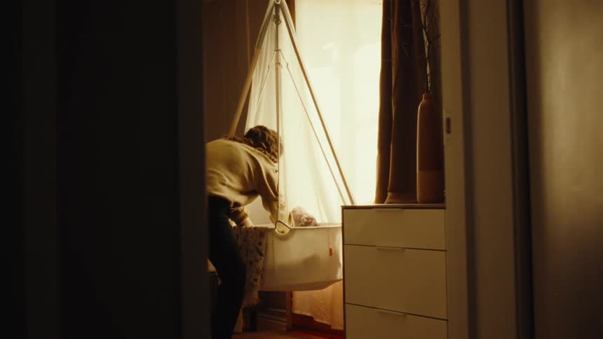 A mother walks into the bedroom and gently picks up her infant