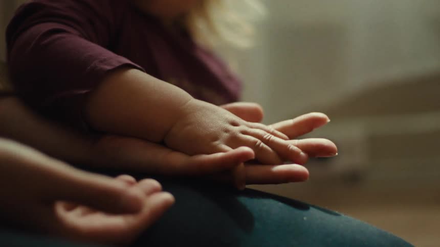 Closeup of an adult holding a toddlers small hands as they play indoors