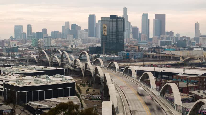 The curved contemporary Sixth Street Viaduct bridge leading toward the Los Angeles skyline filled with skyscrapers