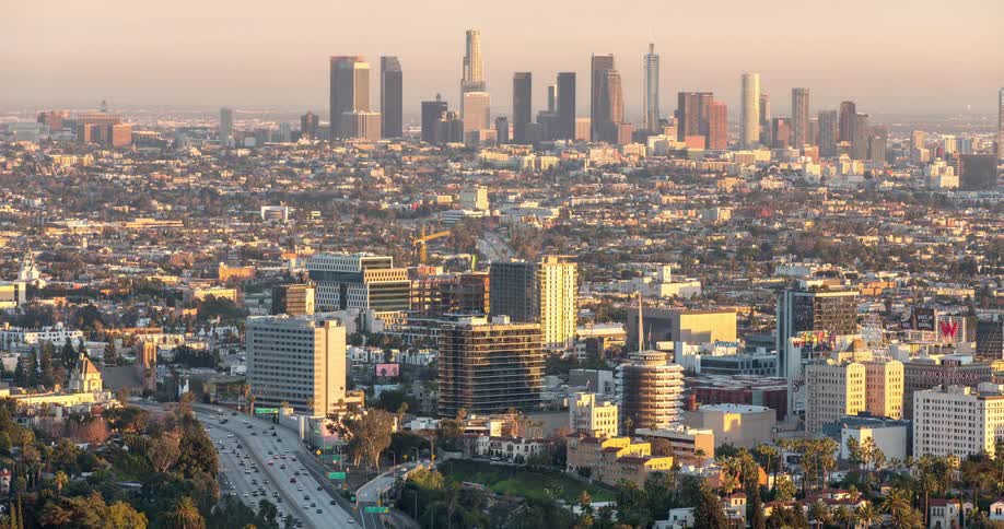 A city skyline rises above a busy road bustling with traffic at midday