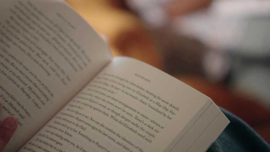Closeup of a hand turning pages while reading a book indoors