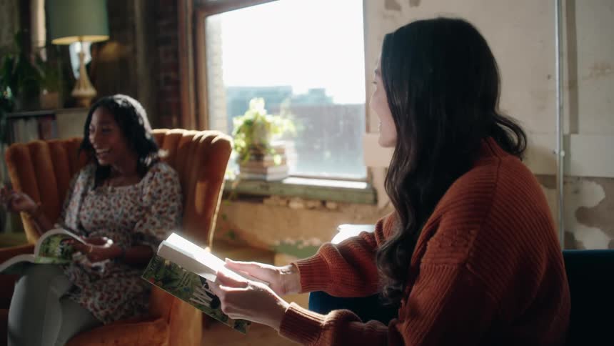 Female friends conversing about a book in a room during daytime