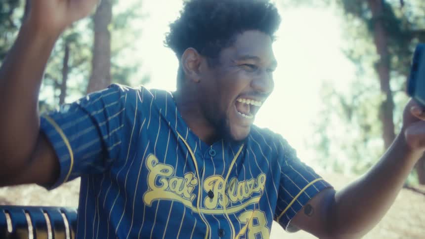Close up of a young black man celebrating as he watches a game on a mobile phone while sitting outdoors during daytime