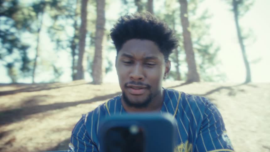 Close up of a young black man making a mobile video call while sitting at a park during daytime