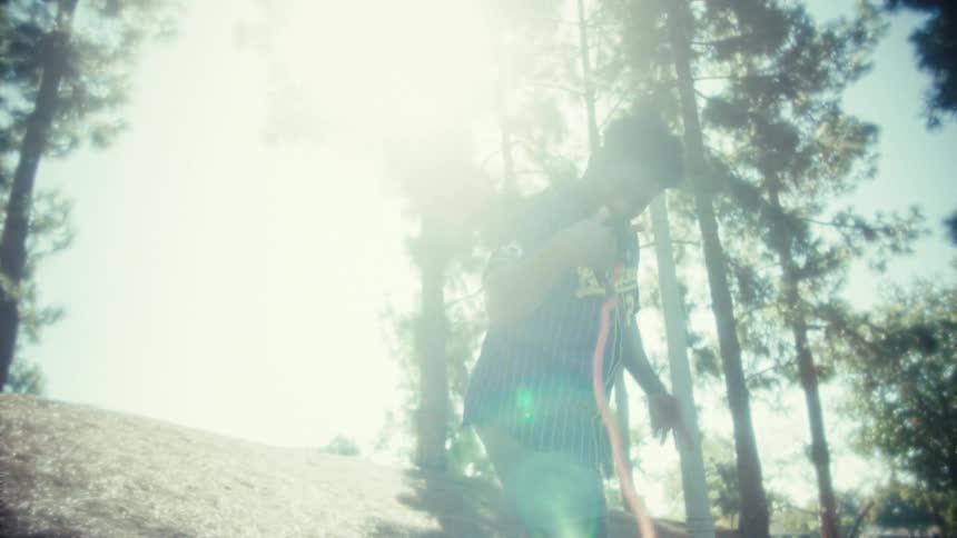 A man wearing a blue and yellow pinstriped jersey with player 28 on the back walks a dog not visible only the red leash up a grassy hill in a sunny park he turns to the camera and smiles broadly before continuing on the paved path