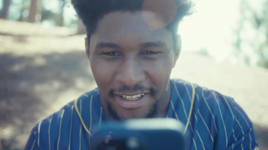 A young black man on a mobile video call while sitting outdoors at a park during daytime