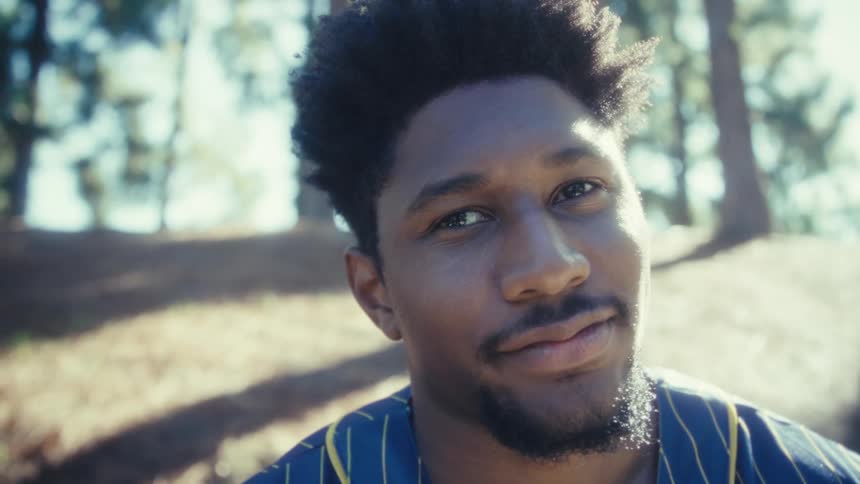 Man smiling while looking at his phone in a sunlit outdoor area
