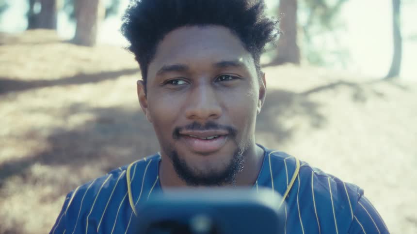 Man smiling while looking at his smartphone in a sunny outdoor setting
