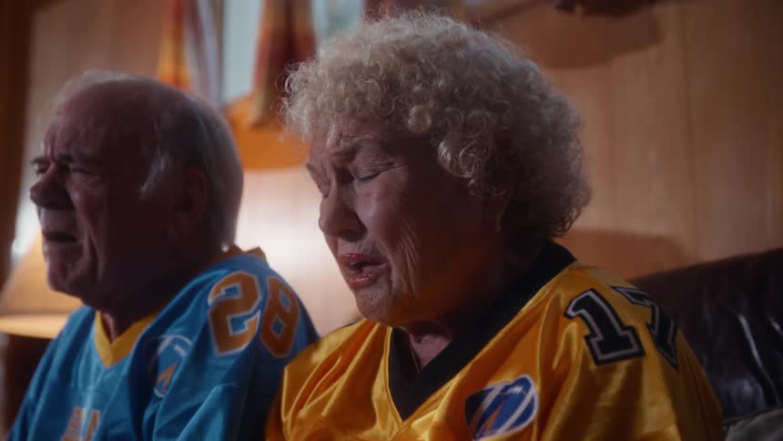 An elderly couple expressing sad emotions while watching a sports game in a living room during daytime