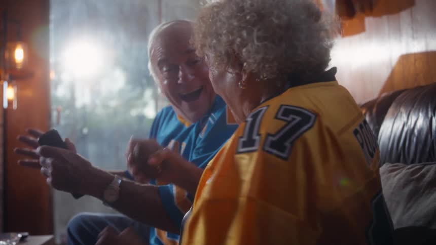 Older couple excitedly watches a football game while sitting in their living room