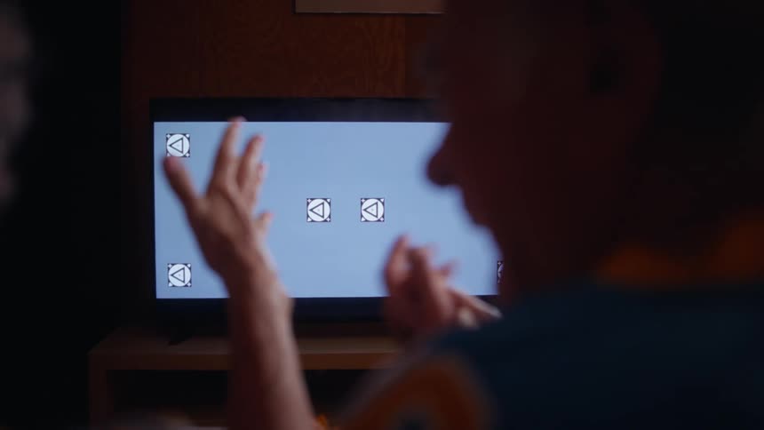 The man and woman clap while watching sports on the television