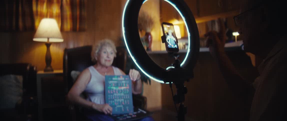 Elderly woman being recorded by a smartphone on a ring light while presenting a chart sheet
