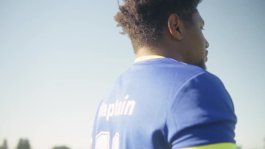 Man in blue and yellow sports shirt gazes into distance on open field under sunny sky
