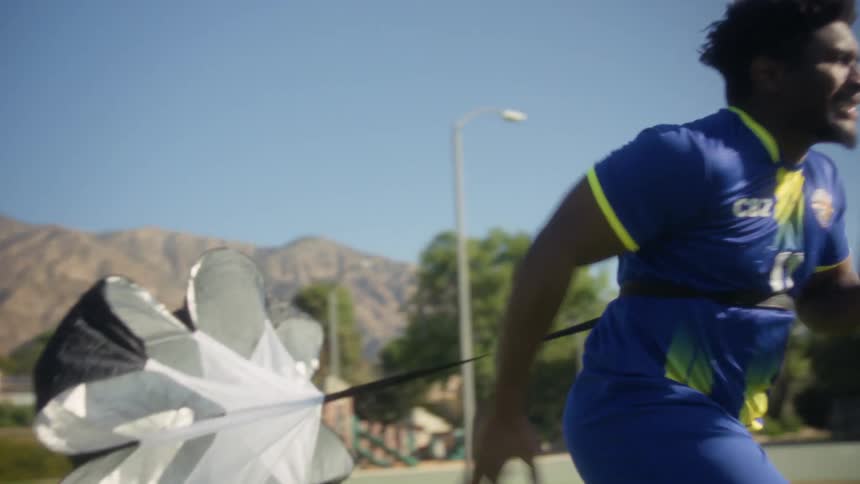 The man is running with a small parachute hooked to his back