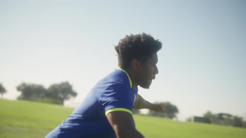 A young black male wearing a cbz jersey trains on a soccer field under the bright sun