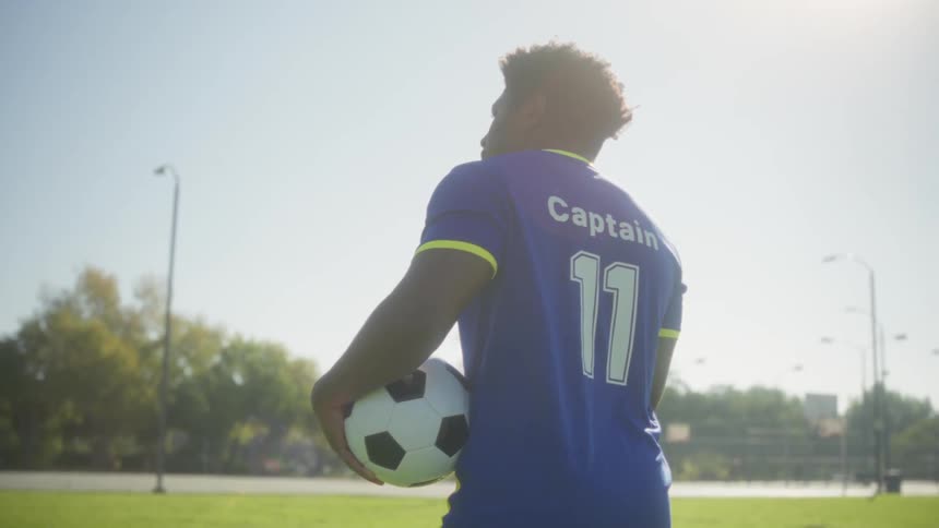 Young black man walking on a soccer field carrying a ball under his arm outdoors during day time