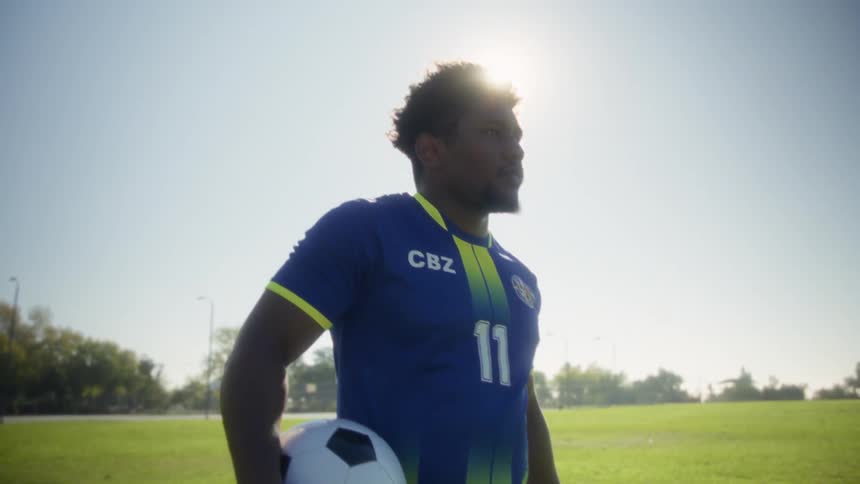 Soccer player walking across the field with a ball under strong sunlight