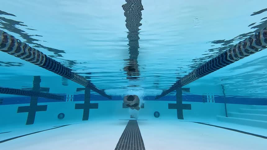 The woman is swimming underwater in the pool
