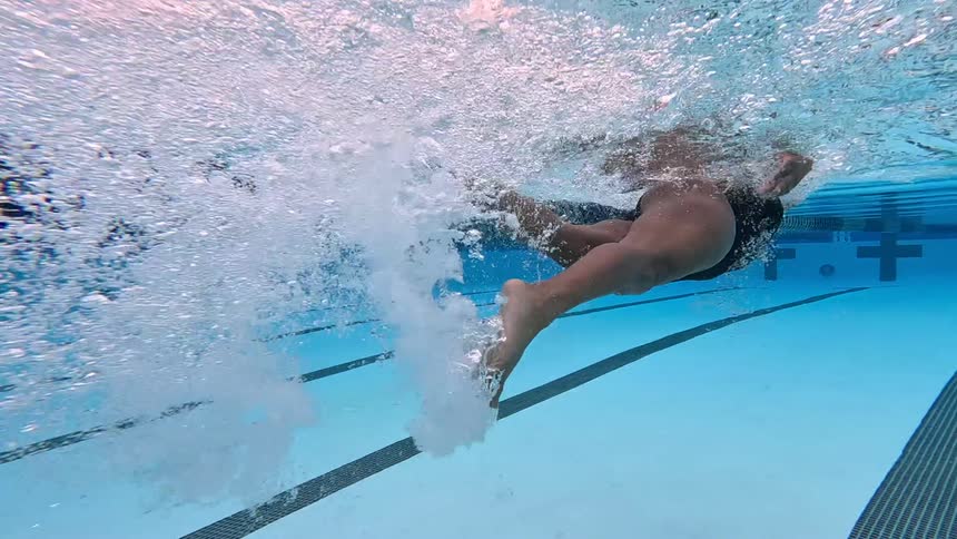 This underwater view captures a swimmer performing the freestyle stroke seen primarily from the waist down moving from left to right across the lanethe swimmers powerful flutter kick generates a significant amount of white bubbles and churn