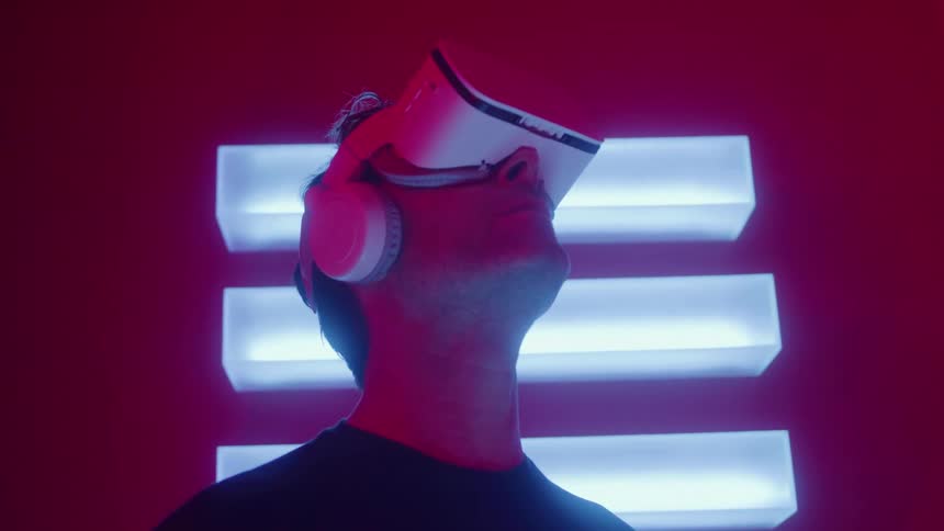 A man wears a vr headsetin a red room under vibrant blue neon lighting immersed in a virtual experience