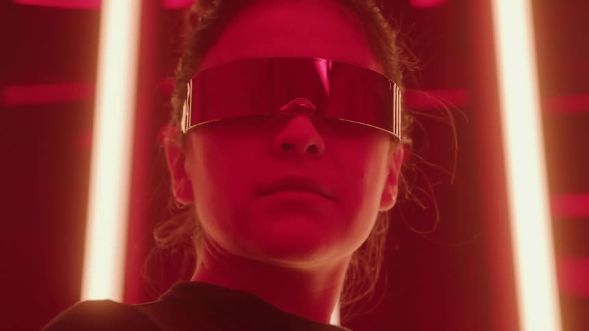 Young adult woman wearing futuristic goggles on a room with colorful lights indoors