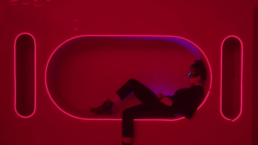 Woman wearing digital shades and a fashionable outfit reclines in a light outlined recessed nook
