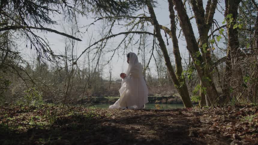 An indian woman dressed in white kneels in prayer near a river in the woods