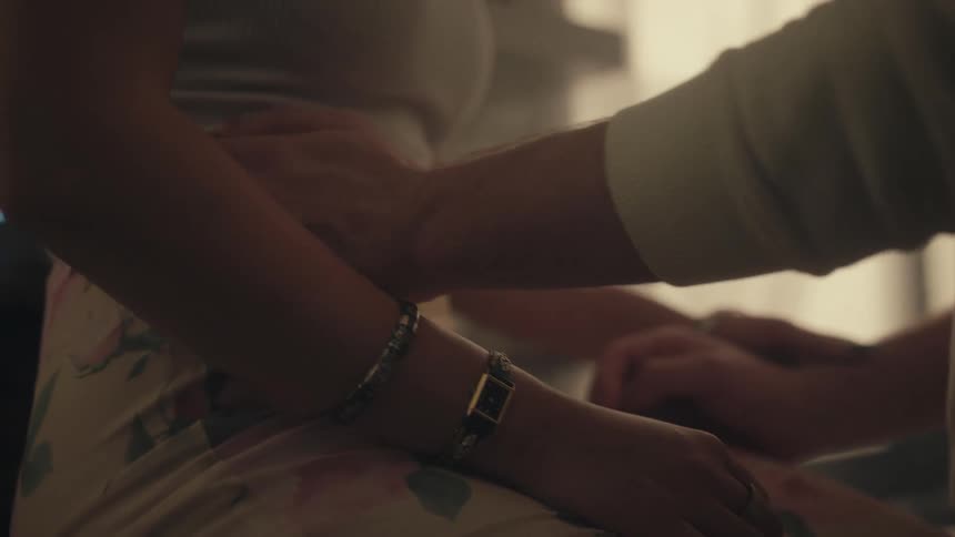 Young man holding hands and caressing the arms and body of a young woman sitting down in front of him indoors during day time