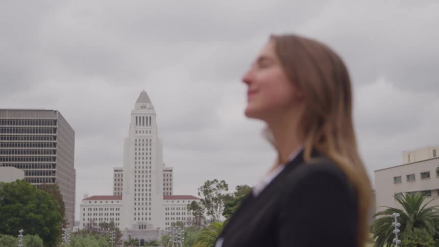 Young adult woman standing and smiling with high rises on the background in a metropolitan area outdoors during day time