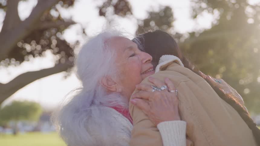 Elderly woman hugging someone in a sunlit outdoor area