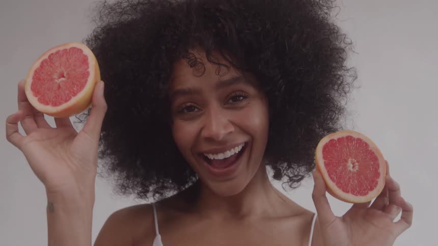 A woman is being silly and holds two grapefruit halves up to her face like eyes
