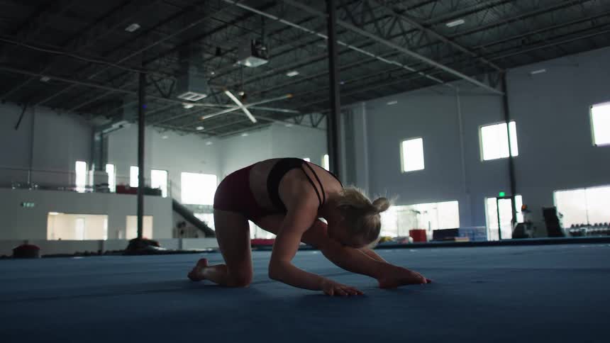An athletic female leans forward while stretching in a gymnasium