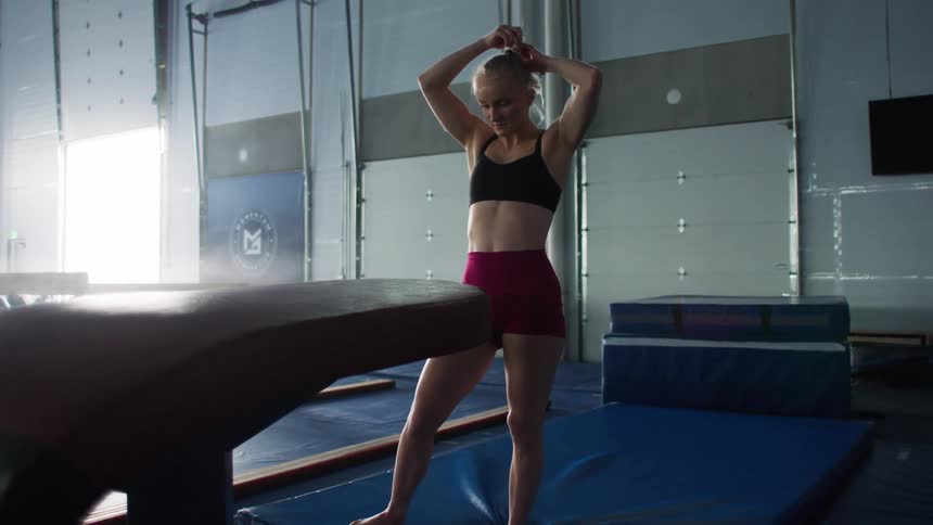 Gymnast fixing her hair beside a vault apparatus in a gym