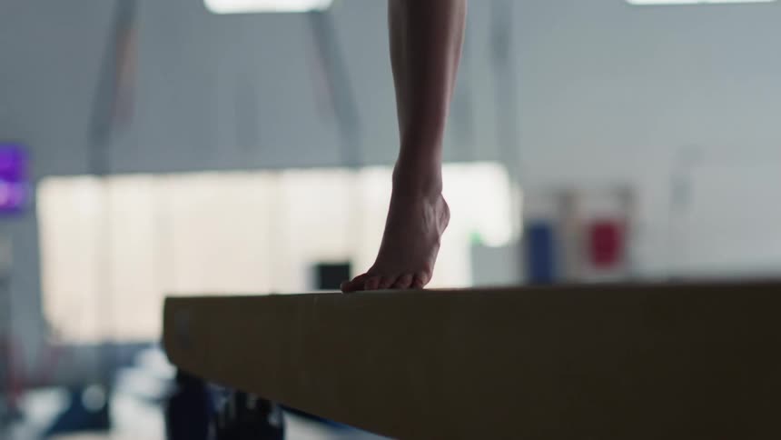 Female gymnast performs a turn during a balance beam routine in the daytime