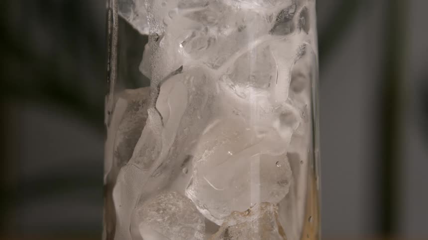 Acloseup shot shows condensation and textured ice cubes filling a clear sweating glass against a blurry indoor background