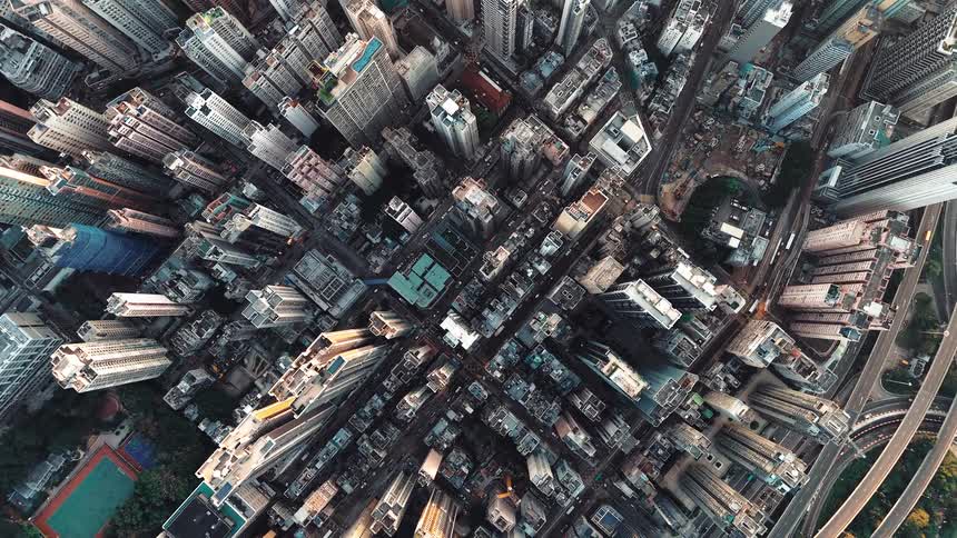 An extreme topdown aerial shot captures a dizzying densely packed urban core showing a vast complex grid of streets surrounded by countless towering residential and commercial skyscrapers