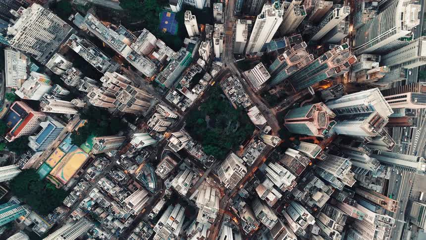 A top down aerial shot shows an extremely dense city with tall buildings and narrow streets circling a small central park area