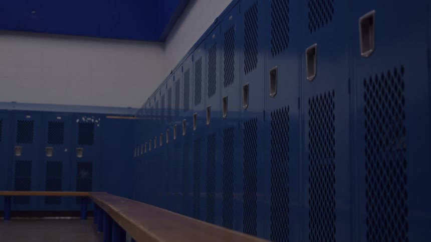 An empty locker room with a wood bench and may metal blue lockers