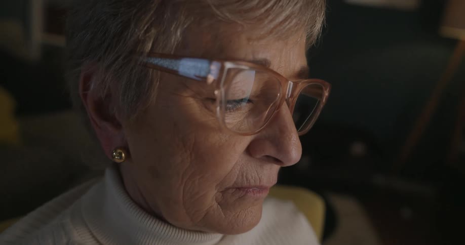 An elderly woman is sitting in a cozy living room reading on her smart phone